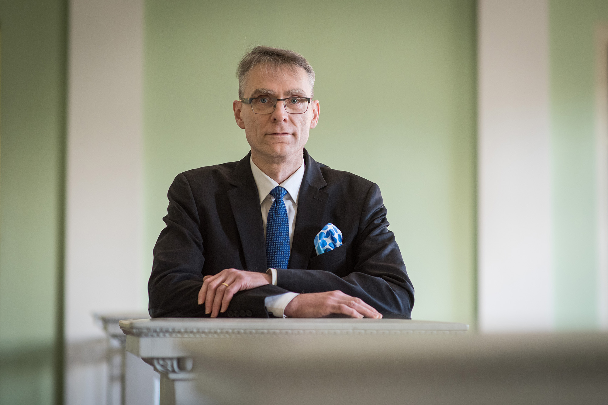 Chancellor of Justice Tuomas Pöysti smiling and wearing a suit in the Government Palace.